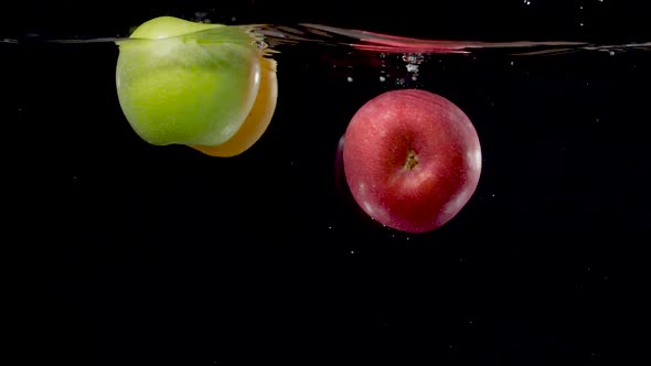 Beautiful yellow, green, and red apples floating in water in slow motion. alt