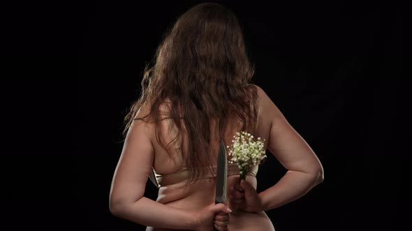 Back View Plus Size Woman in Bra Holding Knife and Bouquet Standing at Black Background alt