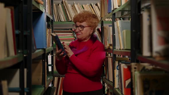 Emotional Elderly Woman in Glasses Found Her Favorite Book on the Shelf Closeup alt