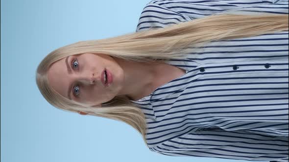 Blonde Young Woman Spreading Her Hands To the Sides and Saying "What" on Blue Background. alt