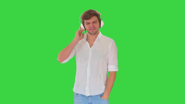 Casual Young Man Listening To Music Holding Headphones By His Hand on a Green Screen, Chroma Key. alt