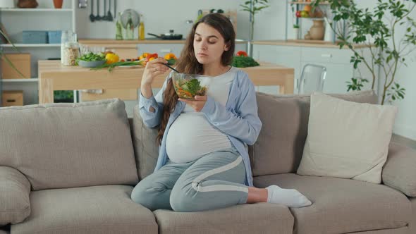 Pregnant Woman With Great Pleasure Eating Vegetable Salad on the Couch alt