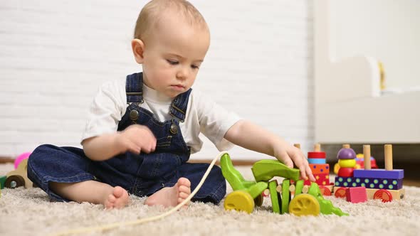 Boy in Denim Overalls Sitting on the Carpet Playing Toys