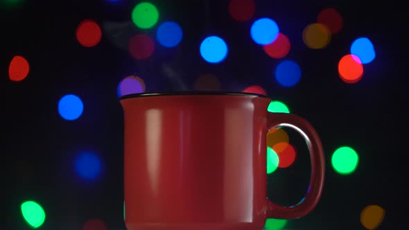 Steaming red mug of coffee or tea over bokeh background