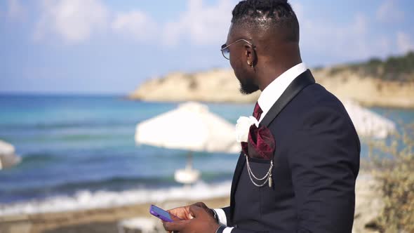 Side View of Confident Happy African American Handsome Man in Suit with Boutonniere Texting on alt