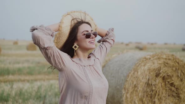 Stylish Lady Relaxes in the Fresh Windy Air Among the Fields with Haystacks alt