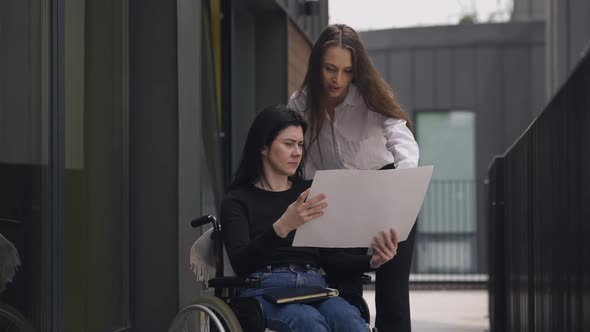 Disabled Caucasian CEO in Wheelchair Discussing Business Project with Assistant Outdoors alt