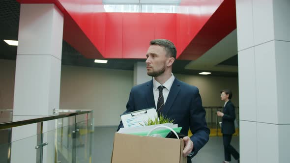 Slow Motion of Unhappy Young Man Leaving Work with Box of Things After Dismissal alt