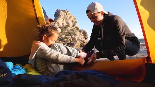 Mom Helps Daughter Puts Her Shoes While She Sits in Camping Tent at Beach