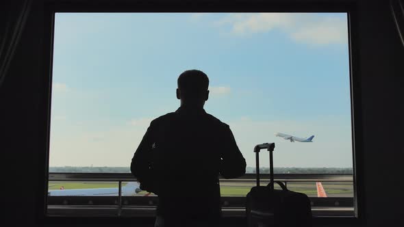 A Young Man Watches the Airplane Take Off From the Window of His Hotel Room alt