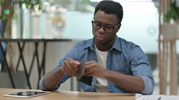 Young African Man Checking Empty Wallet While Sitting in Office alt