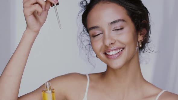 Beautiful Girl with Perfect Skin Dropping Oil Serum in Front of Her Face and Smiling alt