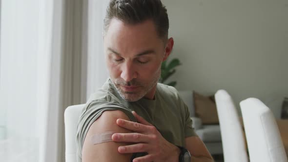 Portrait of caucasian man with vaccinated shoulder smiling and showing ok sign at home alt