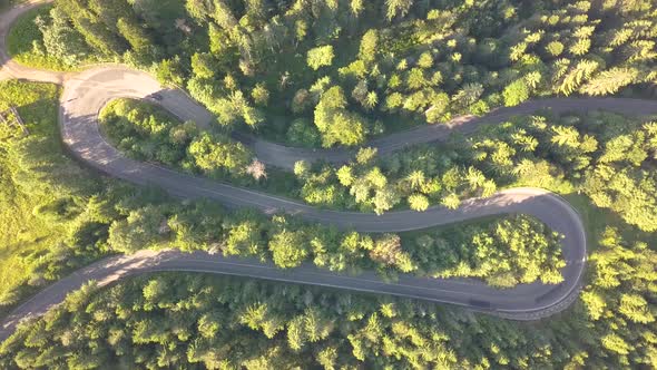 Aerial view of winding road with mowing cars and trucks in high mountain pass trough dense woods. alt