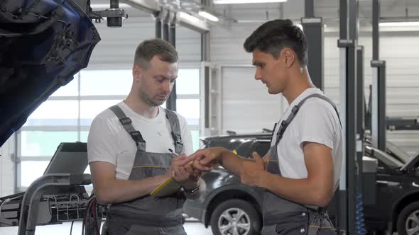 Young Male Car Mechanic Talking To His Colleague at the Garage