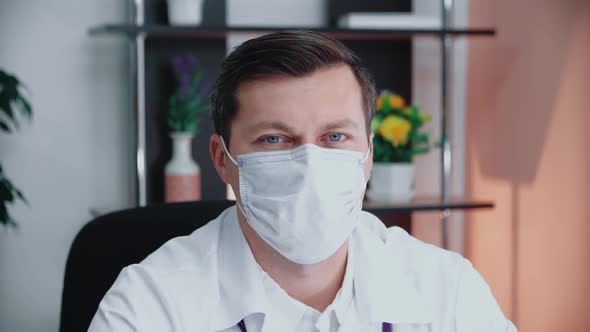 Portrait of a male doctor in a mask sitting in the office. 