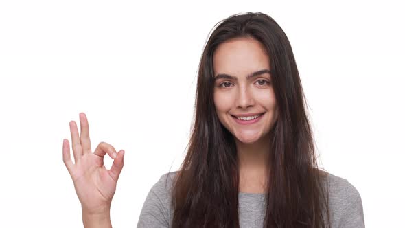 Portrait of Cute Brunette Woman with Long Hair Looking at Camera Smiling Showing OK Sign Over White alt