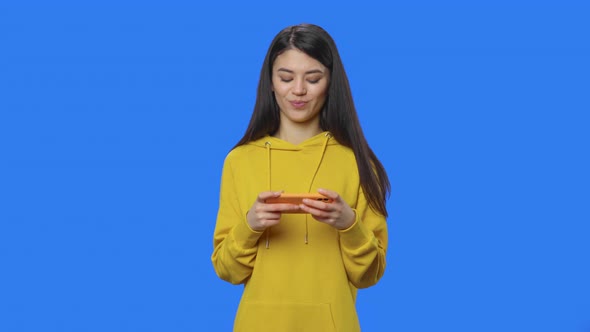 Portrait of Pretty Brunette Enthusiastically Plays a Game on Smartphone alt
