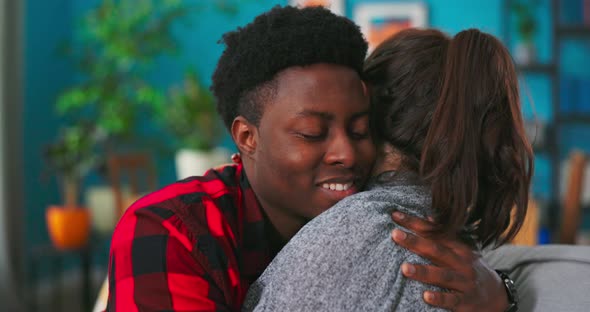 Smiling Happy Couple African Man and American Woman Girl Hugging While Sitting on Sofa at alt