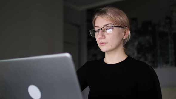 Young business woman in glasses browsing the internet on laptop at home