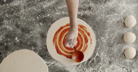 Crop chef smearing tomato sauce on pizza alt