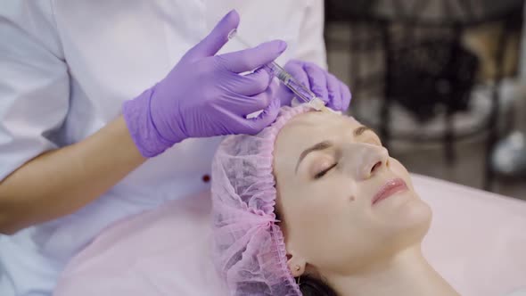A beautiful woman is on the procedure of facial rejuvenation. Beautician makes mesotherapy alt