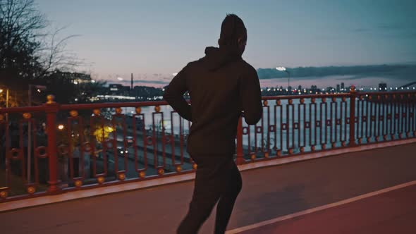 Active African American Man Running on City Bridge Late in Evening Practicing Jog Workout After alt