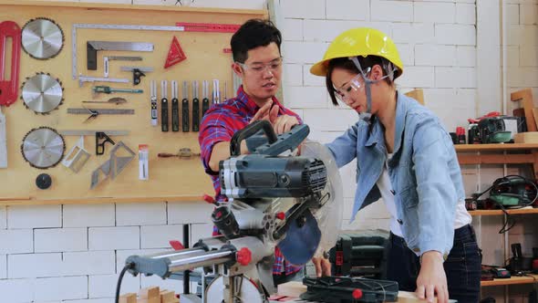 Asian Carpenter man teach trainee in wearing helmet to cut wooden by electric saw in wood workshop