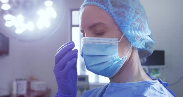 Female caucasian surgeon with face mask, surgical cap and protective clothing in hospital alt