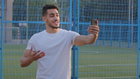 Young Sports Blogger Indian Guy in Sportswear Looking at Smartphone Camera Records Broadcasts From alt