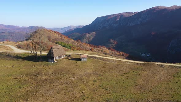 Flying Above Autumn Countryside Mountain Landscape with Wooden Houses, Thatched Roof and Dirt Road alt