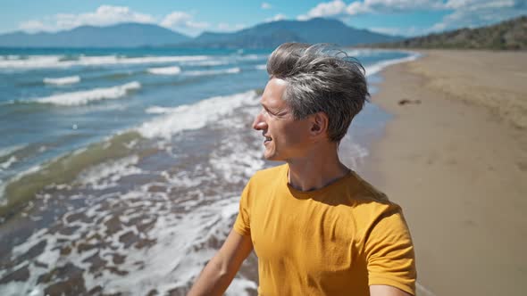 Close Up Portrait of Happy Middle Aged Greyhead Man Walks at Sandy Sea Coast alt