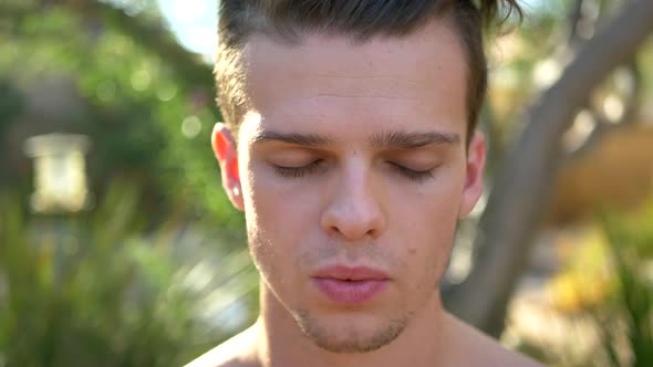 A fit young attractive white man exhaling while closing his eyes and tilting his head down in medita alt