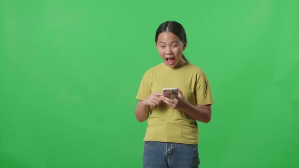 Smiling Kid Girl Use Mobile Phone And Pointing To Smart Phone Screen In Green Screen Studio alt
