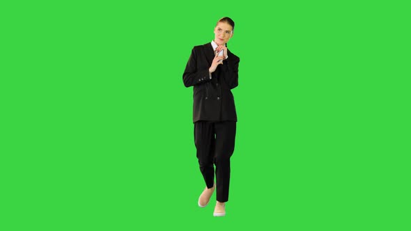Young Woman in Office Suit Walking Typing Some Text on Her Smartphone and Smiling on a Green Screen alt
