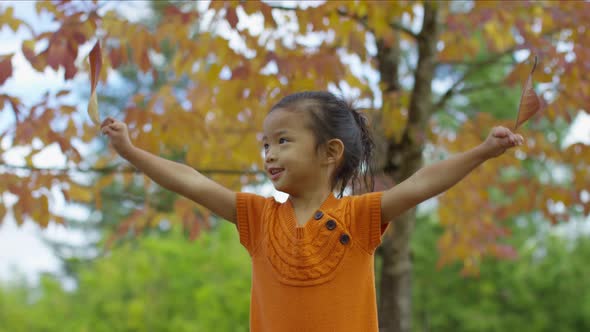 Young girl in Fall spinning with leaves in hands