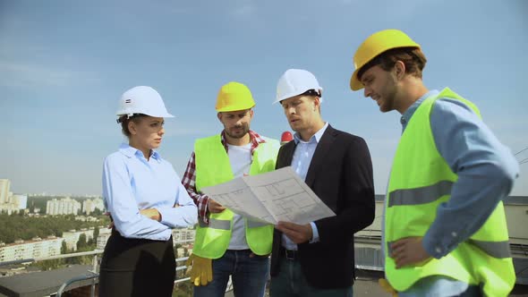 Construction Engineer Holding Architectural Plan Explaining to Workers Helmets