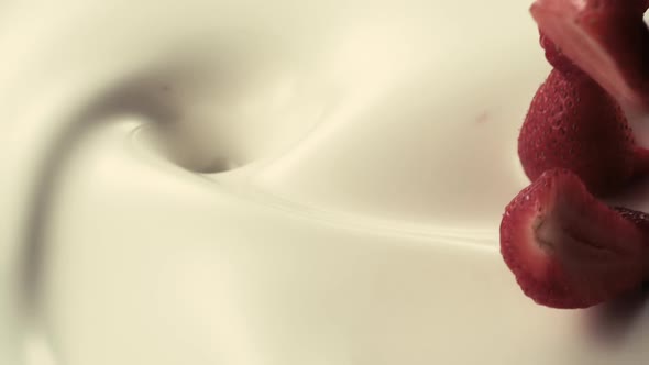 Strawberries fall down into pouring creamy milk in slow motion