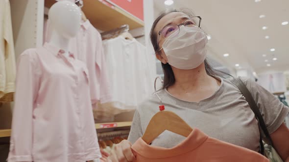 Asian senior woman in medical mask shopping cloth at department store