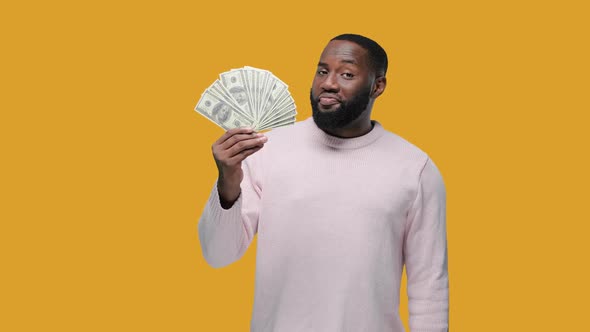 African American Man Handsome Blinking Winking Rich Man Shows a Pack of Dollars on Yellow Background alt