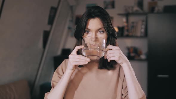 A beautiful girl drinks water from a glass and smiles. Shows the class a thumbs up on the camera.