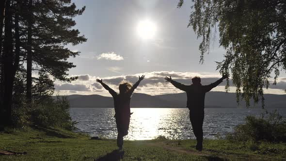 Silhouettes of a Man and a Woman Run To the Lake with Arms Outstretched alt