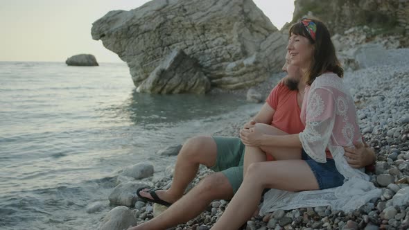 Happy Couple sitting on pebble beach and enjoying the sea view on sunset in Montenegro alt