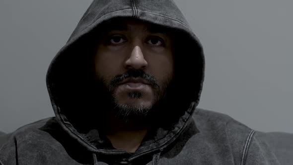 Close up dolly shot of the face of an Indian man wearing a hoodie, his eyes fixed in an intense dete alt