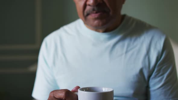 Senior mixed race man sitting in bedroom drinking coffee alt