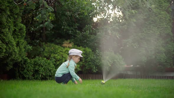 A Girl Plays with Water with a Hose in the Garden Near the House