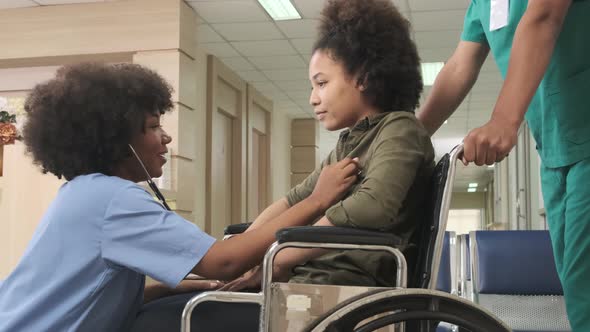 African American female doctor checks patient girl in wheelchair at hospital. alt