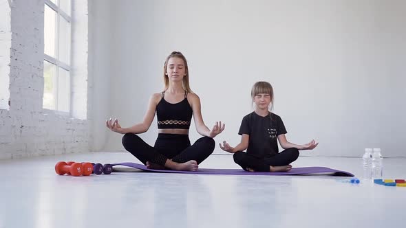 Two Girls-Elder and Younger Sitting on Violet Mats in Lotus Pose with Closed Eyes During Yoga Lesson alt
