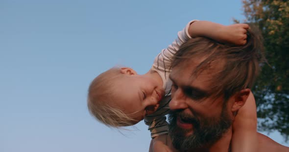 Smiling Baby Boy Sits on Father Neck and Have Fun Together Outdoor in Sunset alt