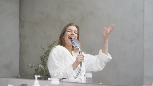 Joyful Caucasian Female in Bathrobe Has Fun in Bathroom Singing